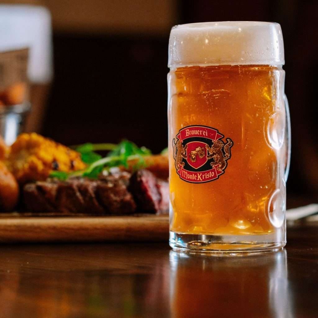 A large glass mug of amber beer beside a plate of grilled meat