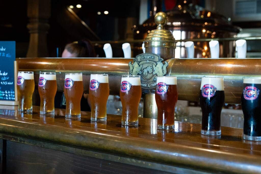 A row of beer glasses lined up on the bar at the brewery, with copper brewing equipment behind