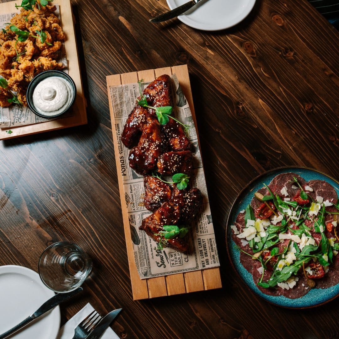 Glazed chicken wings and a salad on a wooden board, seen from above