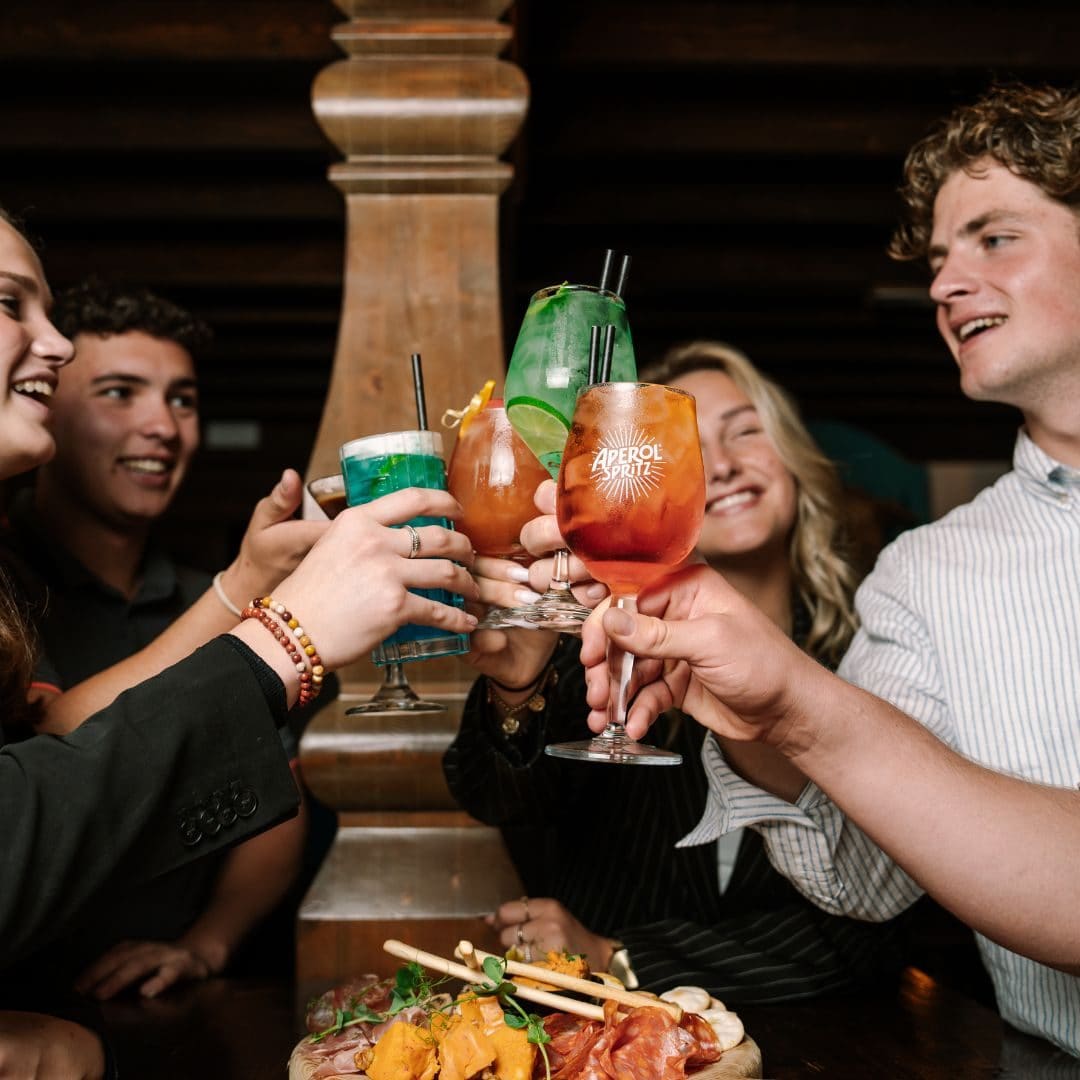 Friends laughing and clinking colourful cocktails together
