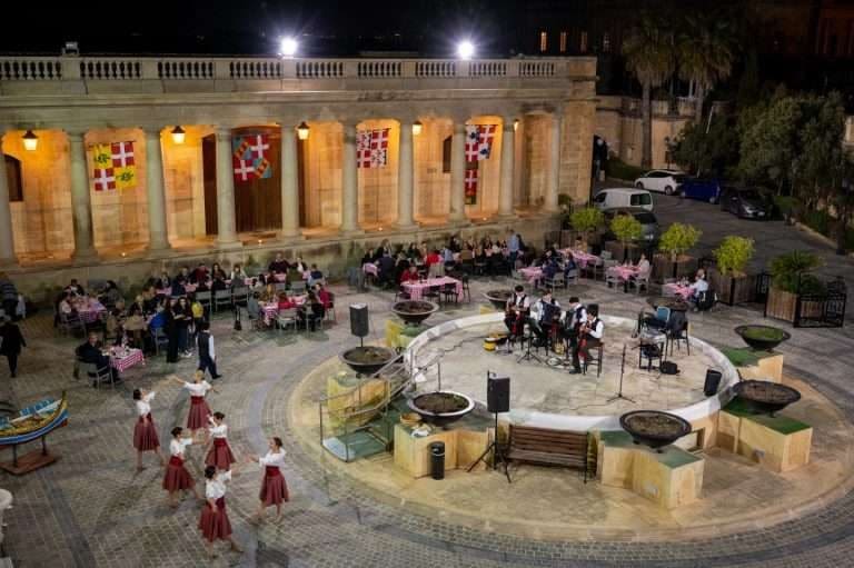 Evening event in Il-Pjazza with folk dancers and tables beneath the colonnade