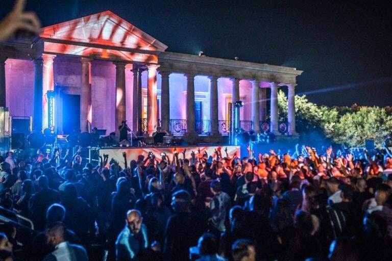 Crowd at a night-time concert in front of a lit colonnaded facade