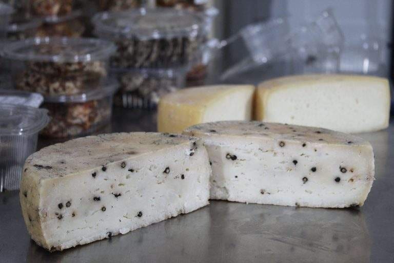 Cut goat cheese wheels flecked with pepper, with other cheeses in the background
