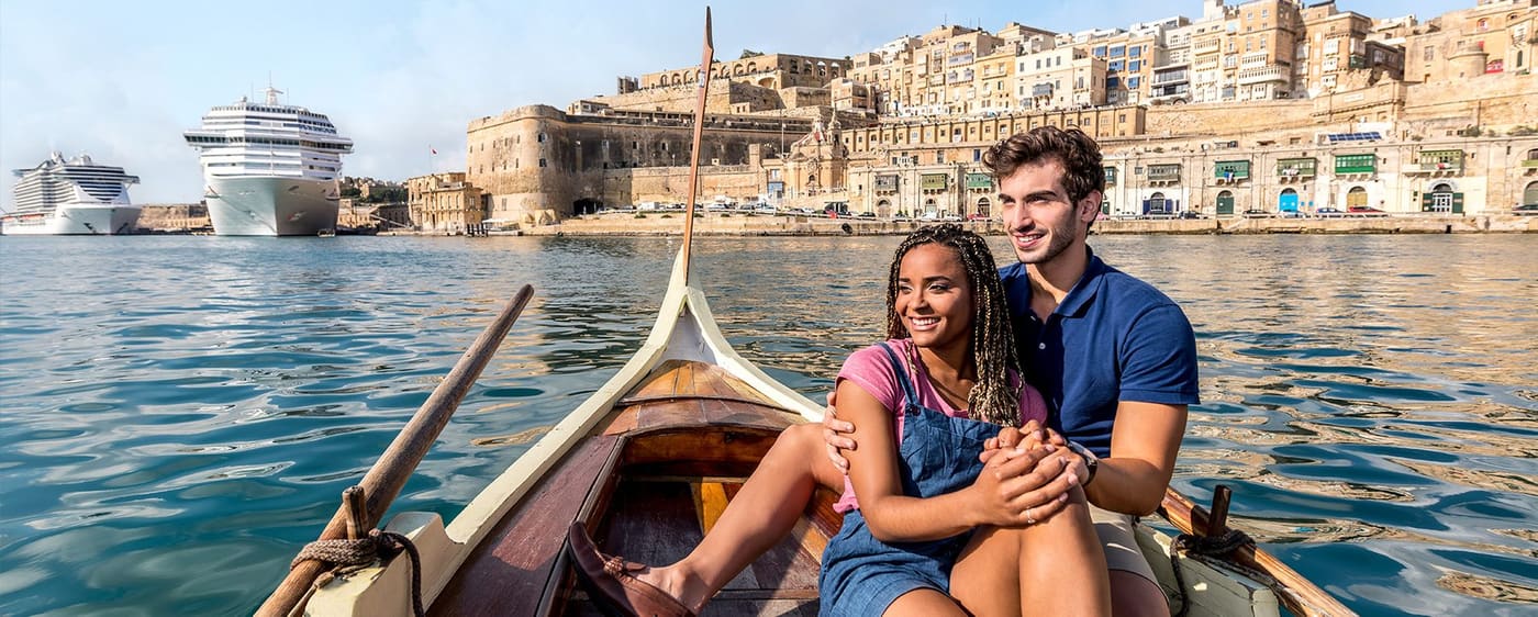 A couple sitting in a traditional Maltese boat on the harbour with Valletta behind