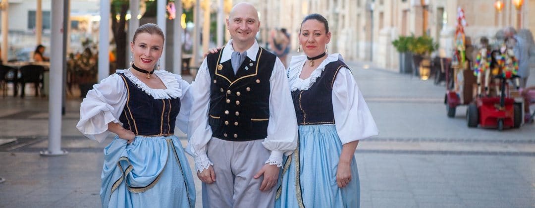 Three performers in traditional Maltese folk costume on the promenade