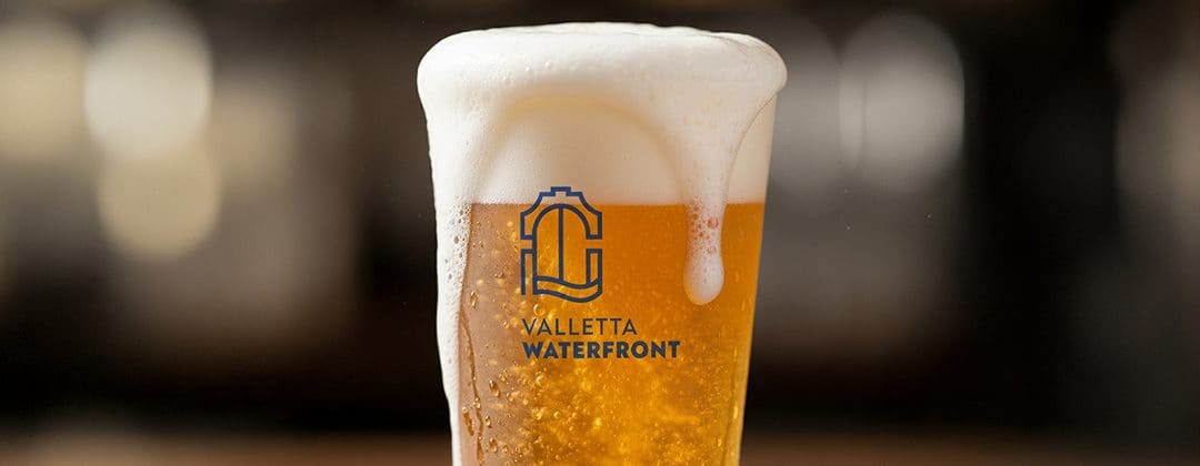 A glass of beer with a foam head in a branded cup