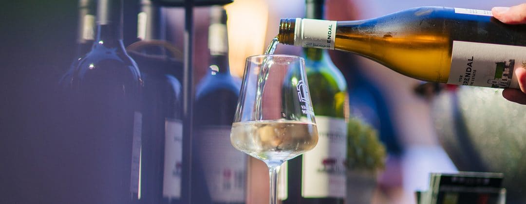 White wine being poured into a glass beside bottles