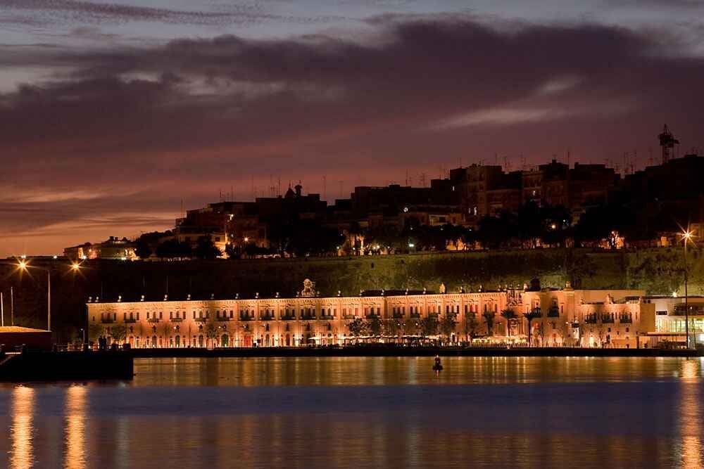 The Valletta Waterfront floodlit at dusk across the Grand Harbour