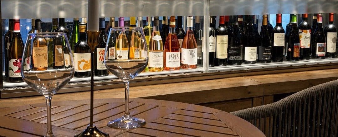 A glass of white wine in front of shelves of bottles at Vinomad