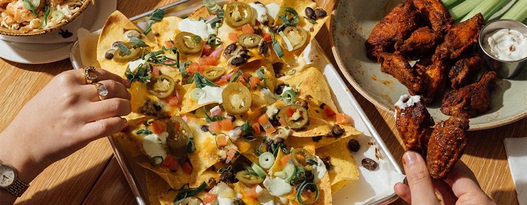 A tray of loaded nachos with jalapenos and chicken wings