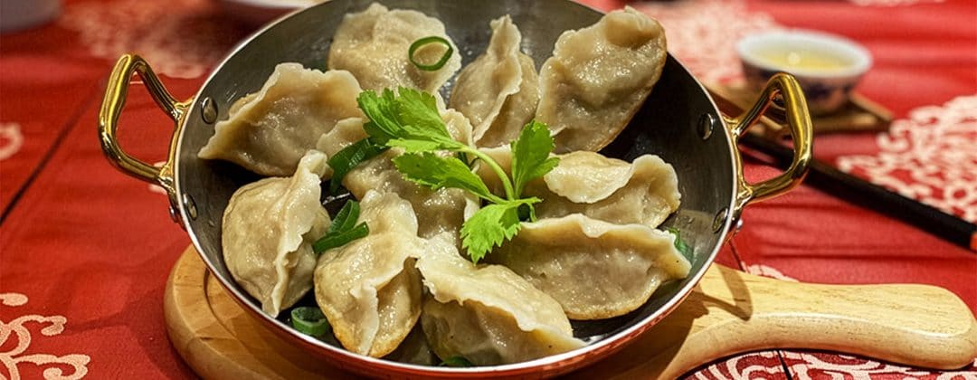 A copper dish of steamed dumplings with coriander