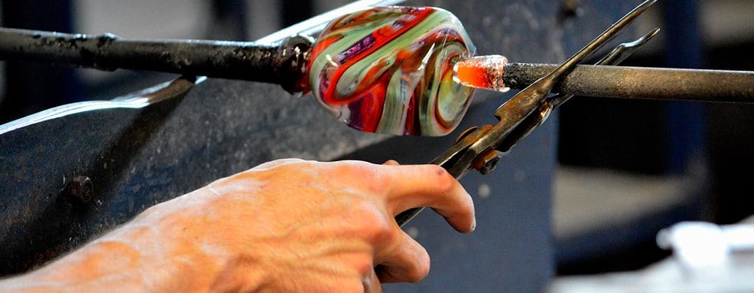 A glassmaker shaping a swirl of molten coloured glass on a blowpipe