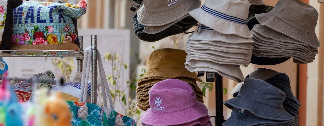 A display of straw hats and caps, including a pink Malta bucket hat